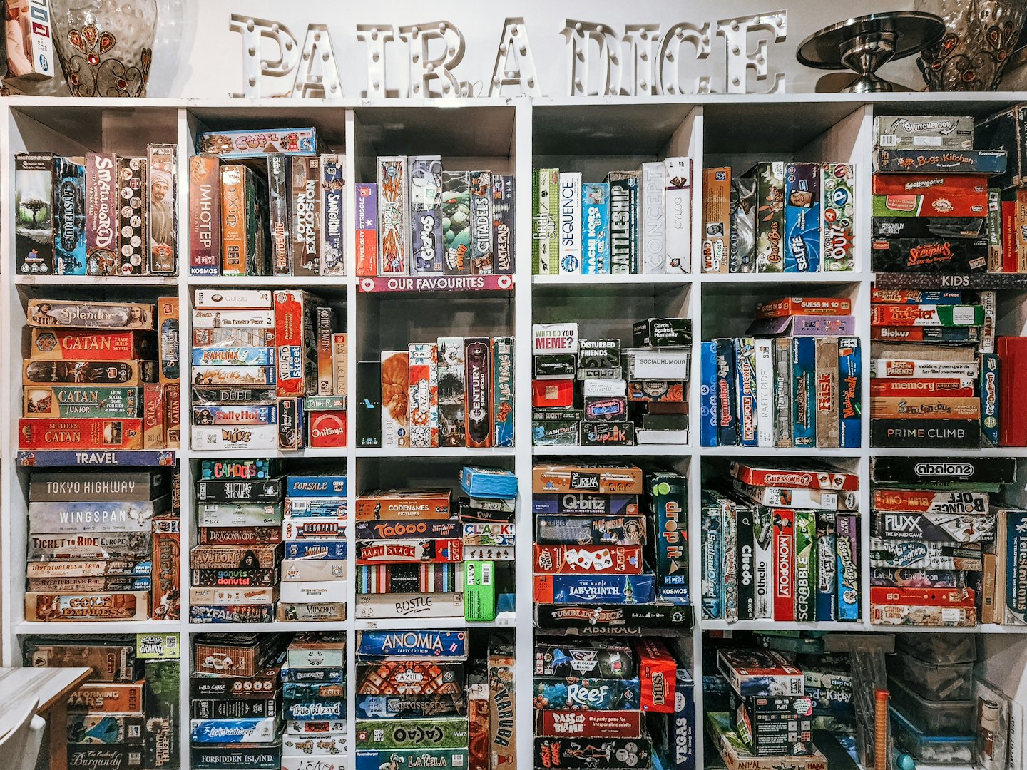 Hundreds of board games organized on white shelves with 'PATRA DICE' sign.